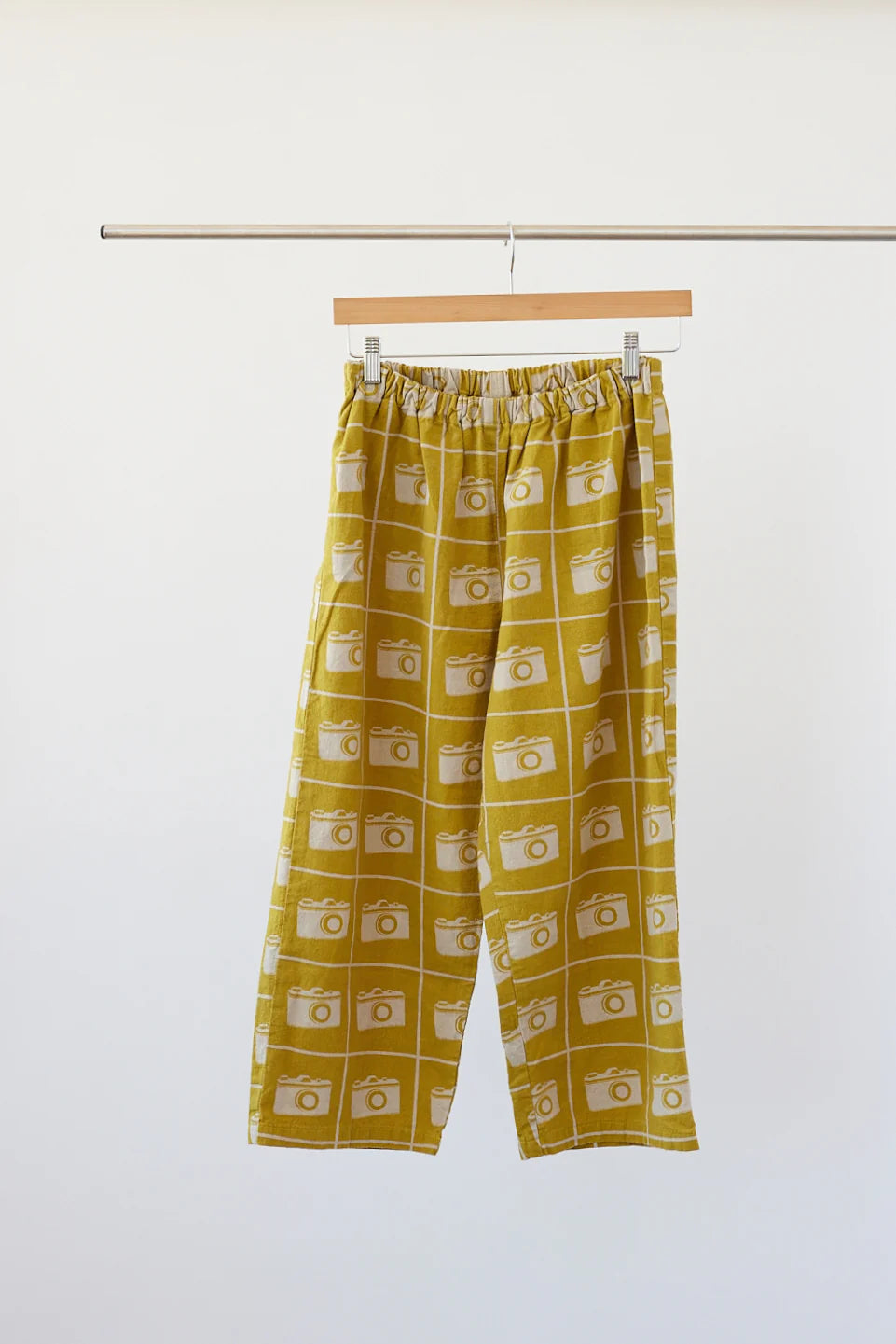 Yellow pants with camera pattern hanging on a rack against a white background