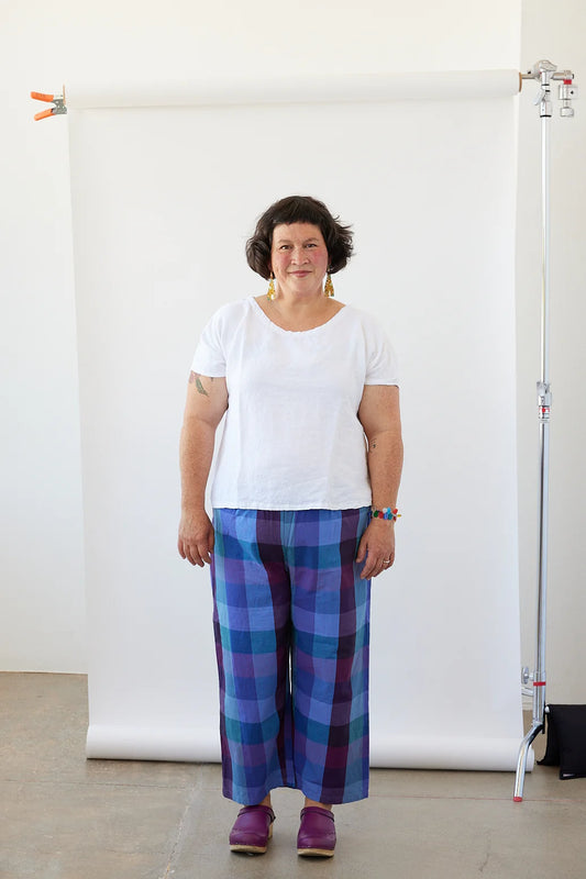 Woman wearing a white shirt and blue plaid pants standing against a white backdrop.