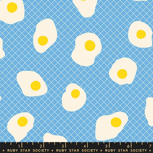 Pattern of fried eggs with yellow yolks on a blue grid background, featuring Ruby Star Society label.