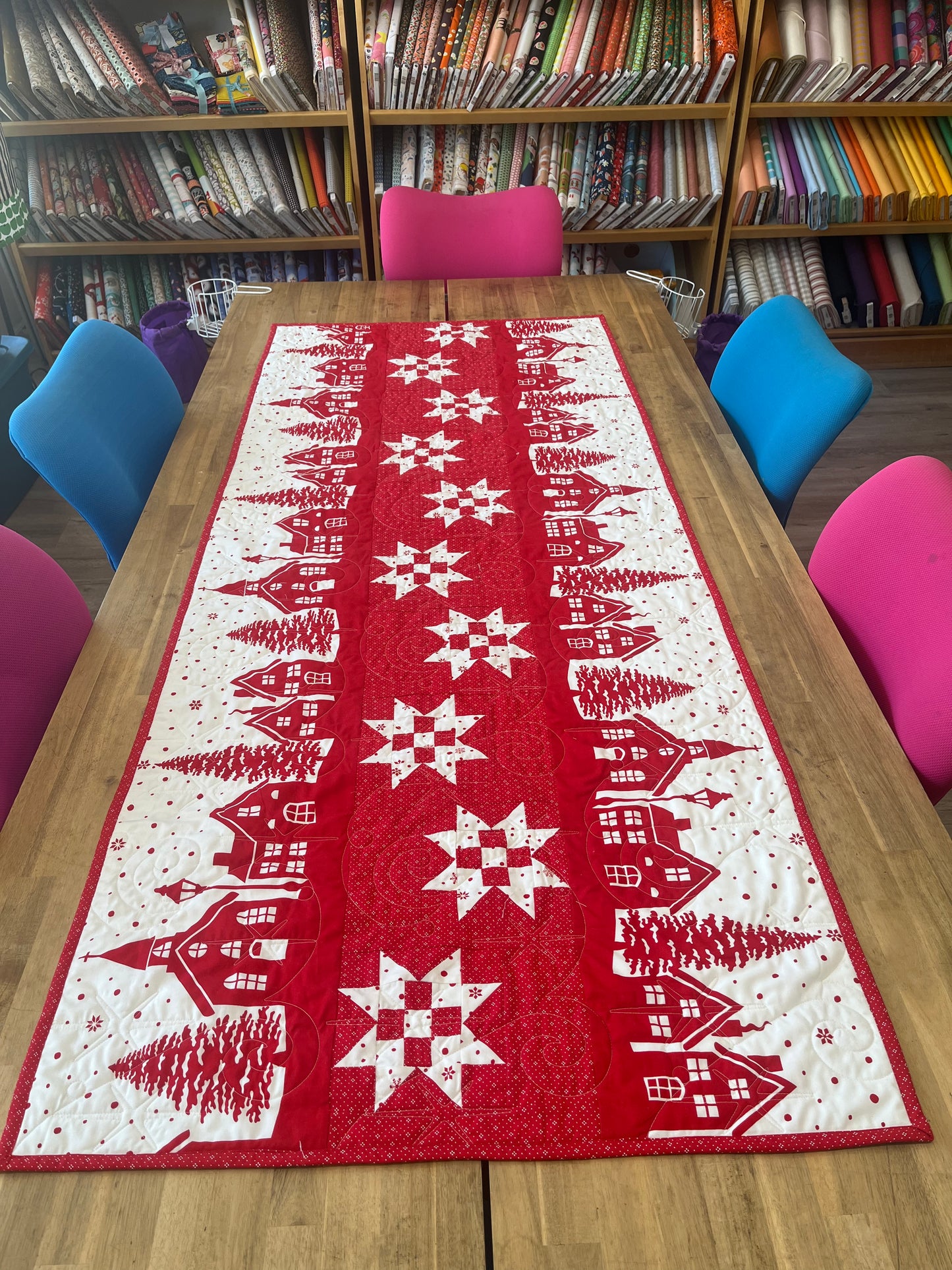 Red table runner with white snowflake and village design on a wooden table.