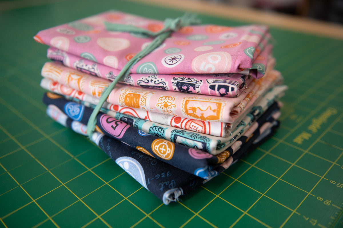 Stack of colorful fabric squares tied with green string on a green cutting mat.