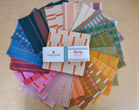 Collection of colorful fabric swatches with a 'Fableism' label on a wooden surface