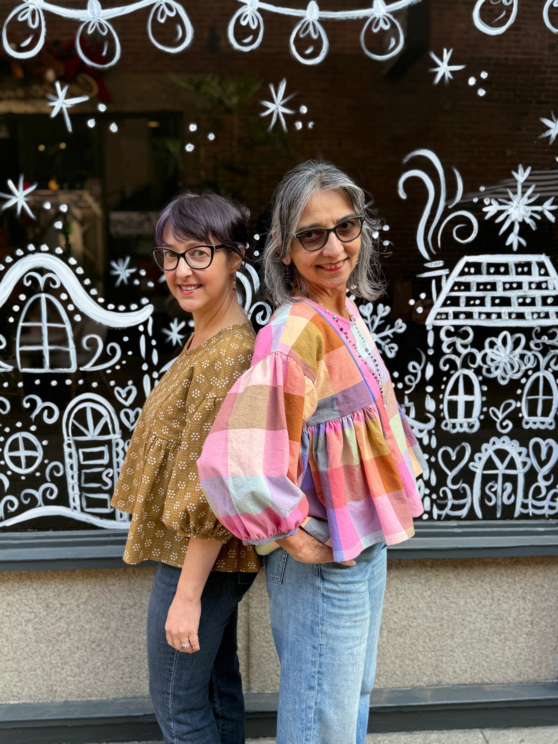Two women wearing handmade shirts posing in front of a window with chalk drawings