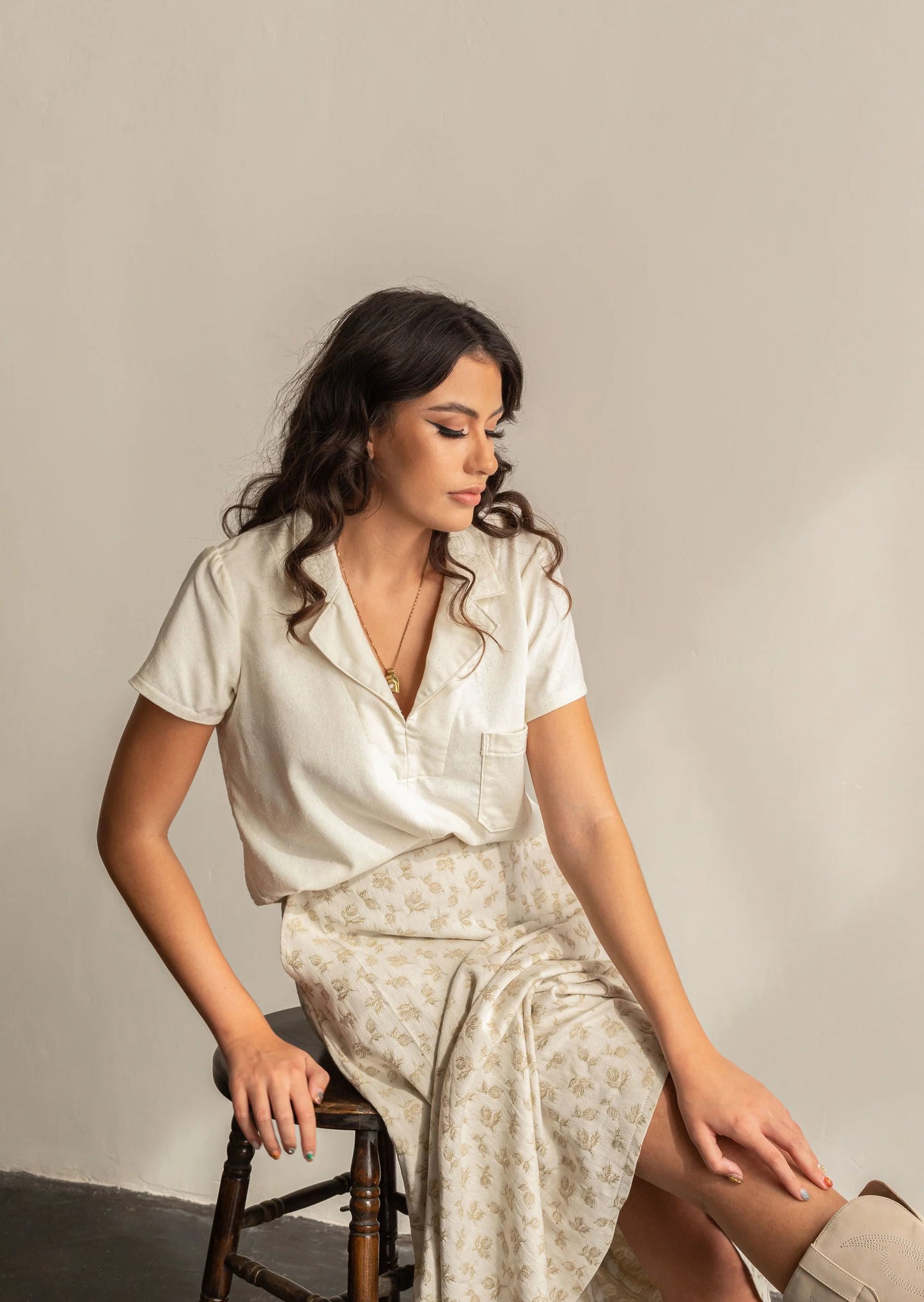 Woman in a white outfit sitting on a chair against a plain background