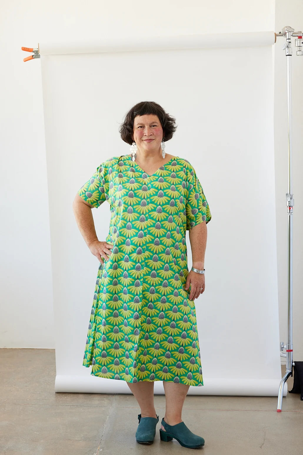 Woman wearing a green patterned dress standing against a white backdrop