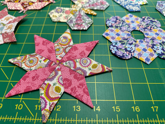 Colorful star-shaped fabric pieces on a green cutting mat with grid lines.