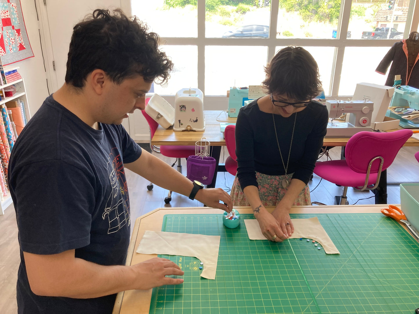 2 people pinning around a curve at a table with a green cutting mat