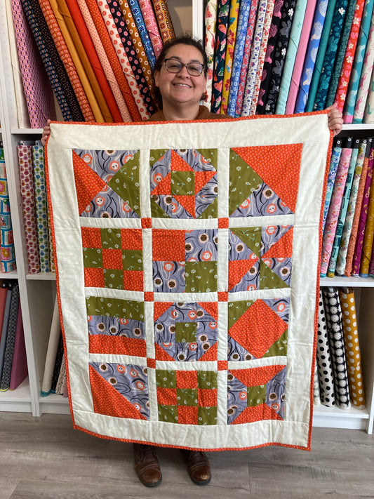 a person holds a finished quilt in orange, green and grey