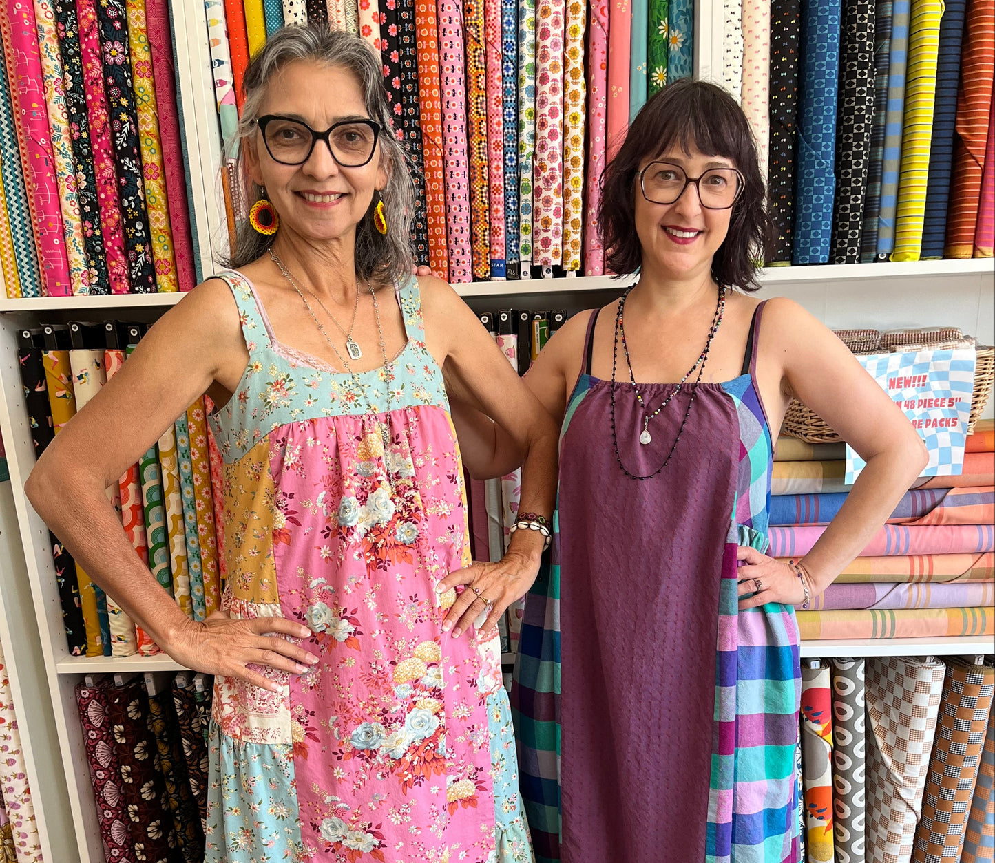Two women wearing colorblock dresses standing in front of a display of colorful fabric rolls.