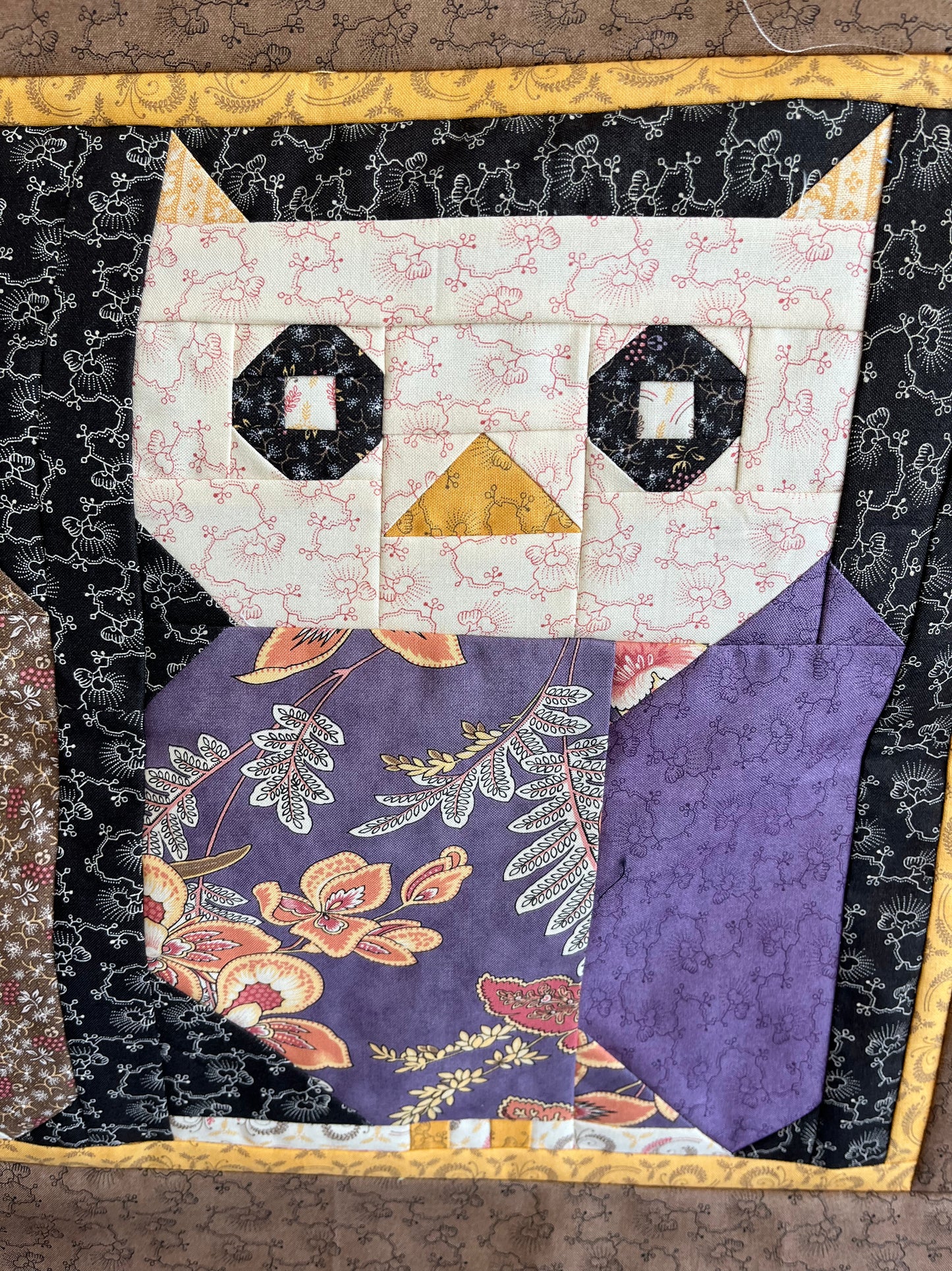 Owl quilt block with floral and geometric patterns on a textured background