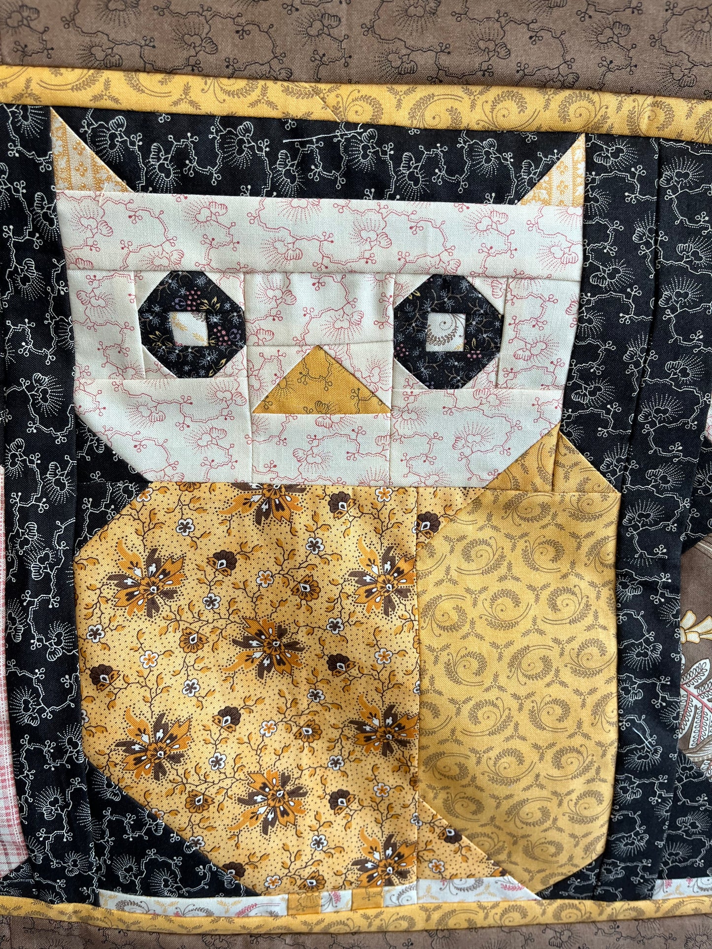 Quilted Owl patchwork design with geometric patterns and floral embellishments on a textured surface.