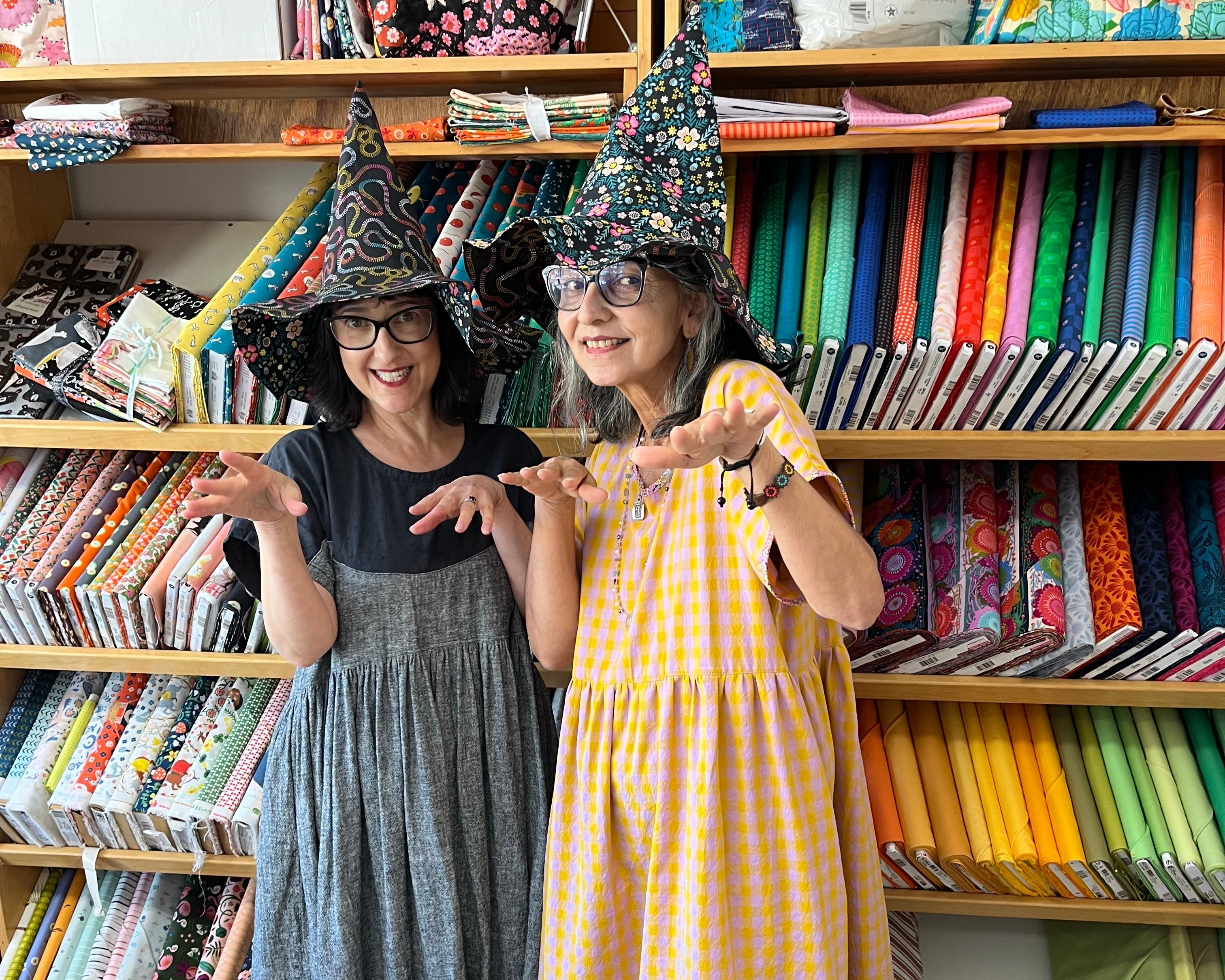Two women standing in front of a bookshelf filled with colorful fabrics and books.