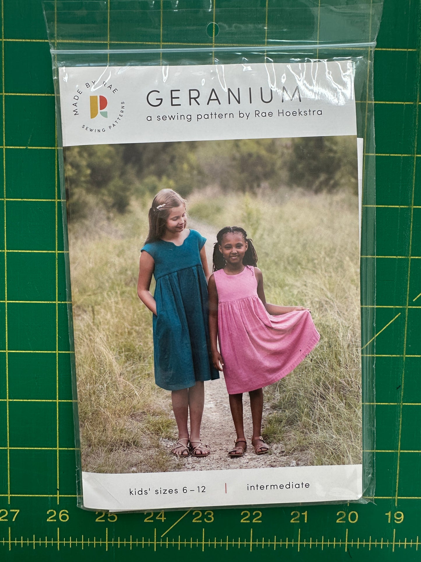 Sewing pattern packaging with two children in dresses on a green grid background