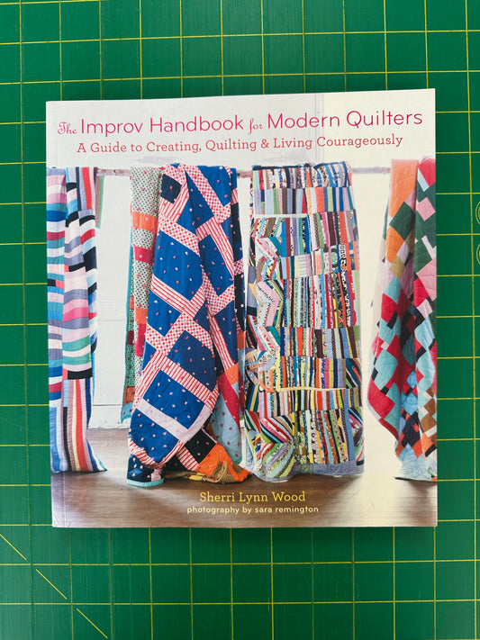 Book titled 'Modern Quilters' on a green cutting mat with quilted fabric samples.