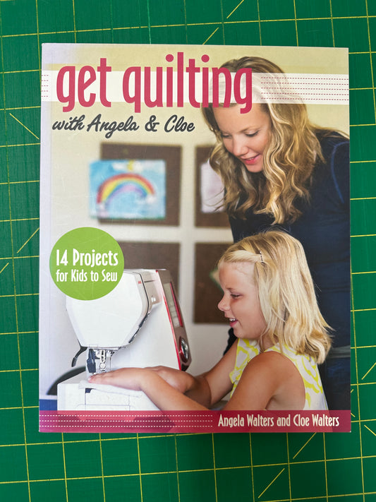 Book titled 'Get Quilting with Angela & Clee' on a green cutting mat.