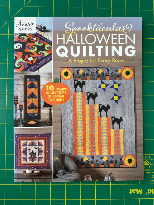 Book cover of 'Spooktacular Halloween Quilting' by Annie's Quilting on a green cutting mat.