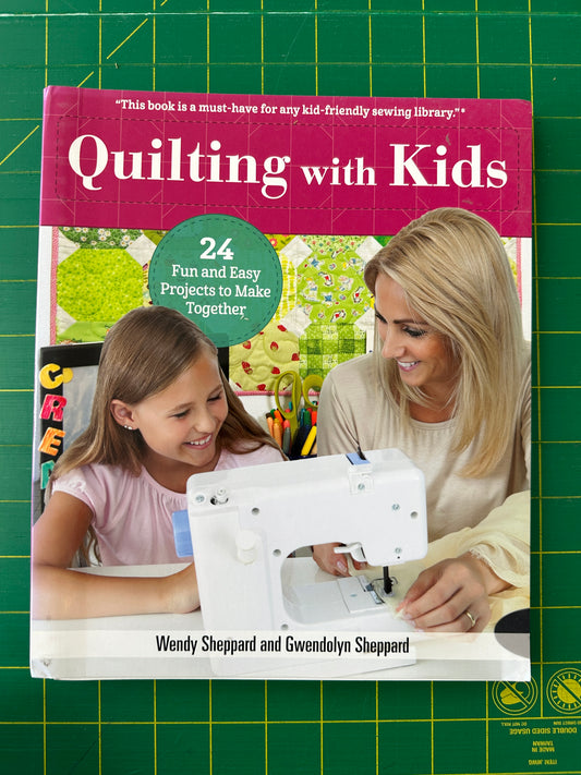 Book titled 'Quilting with Kids' on a green cutting mat