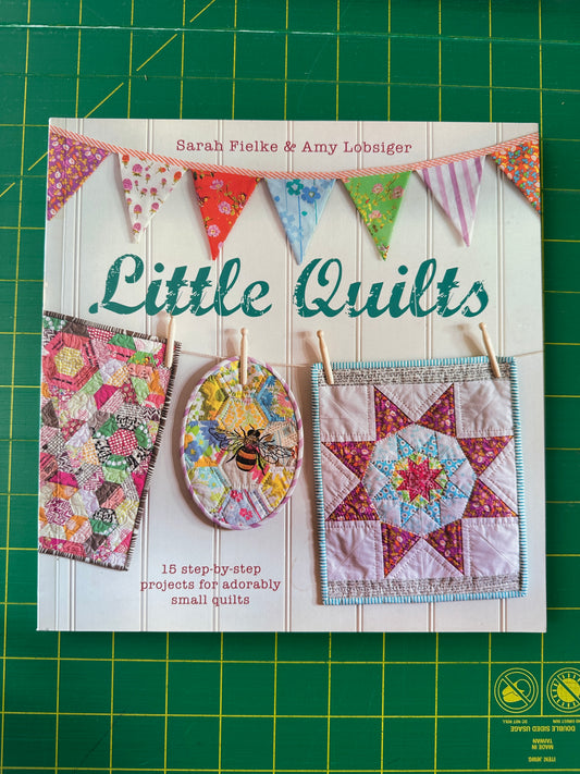 Book cover of 'Little Quilts' with colorful quilt designs on a green cutting mat.