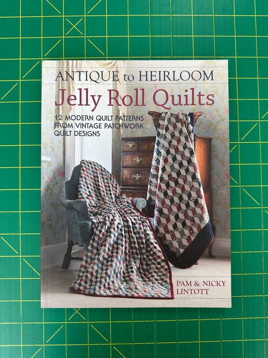 Book titled 'Antique to Heirloom Jelly Roll Quilts' on a green cutting mat with grid lines.