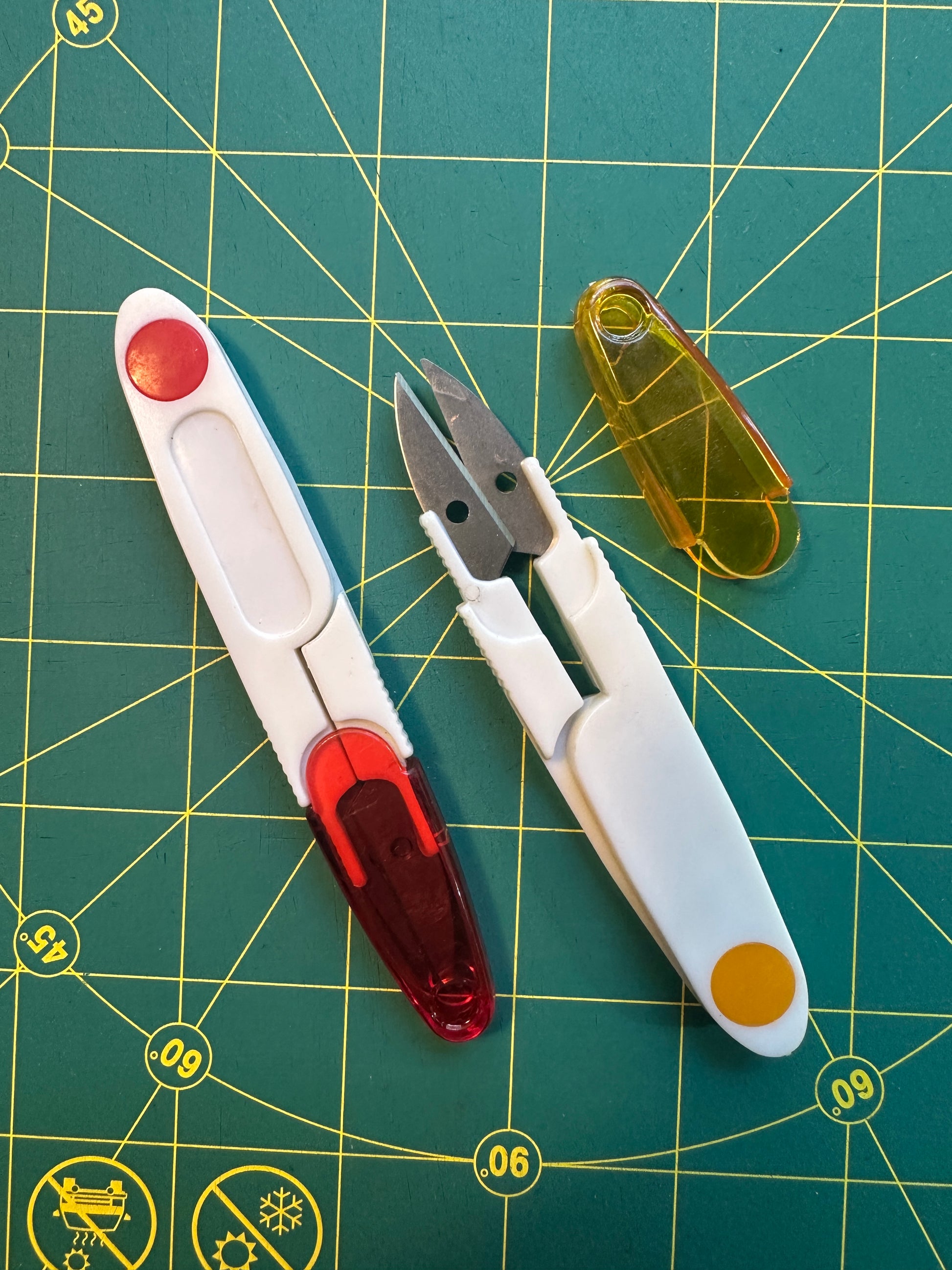 Two thread clippers on a green cutting mat with grid lines