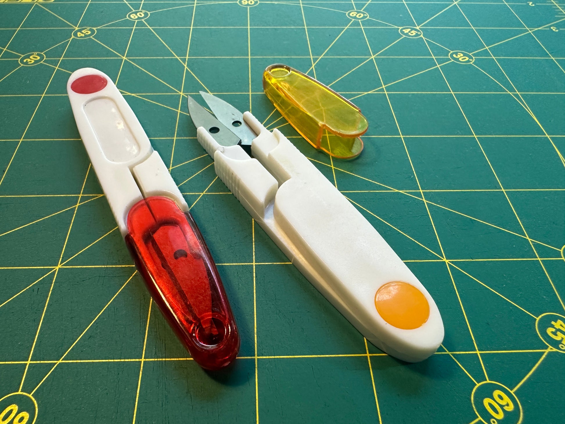Scissprs with a red blade and white handle on a green cutting mat.