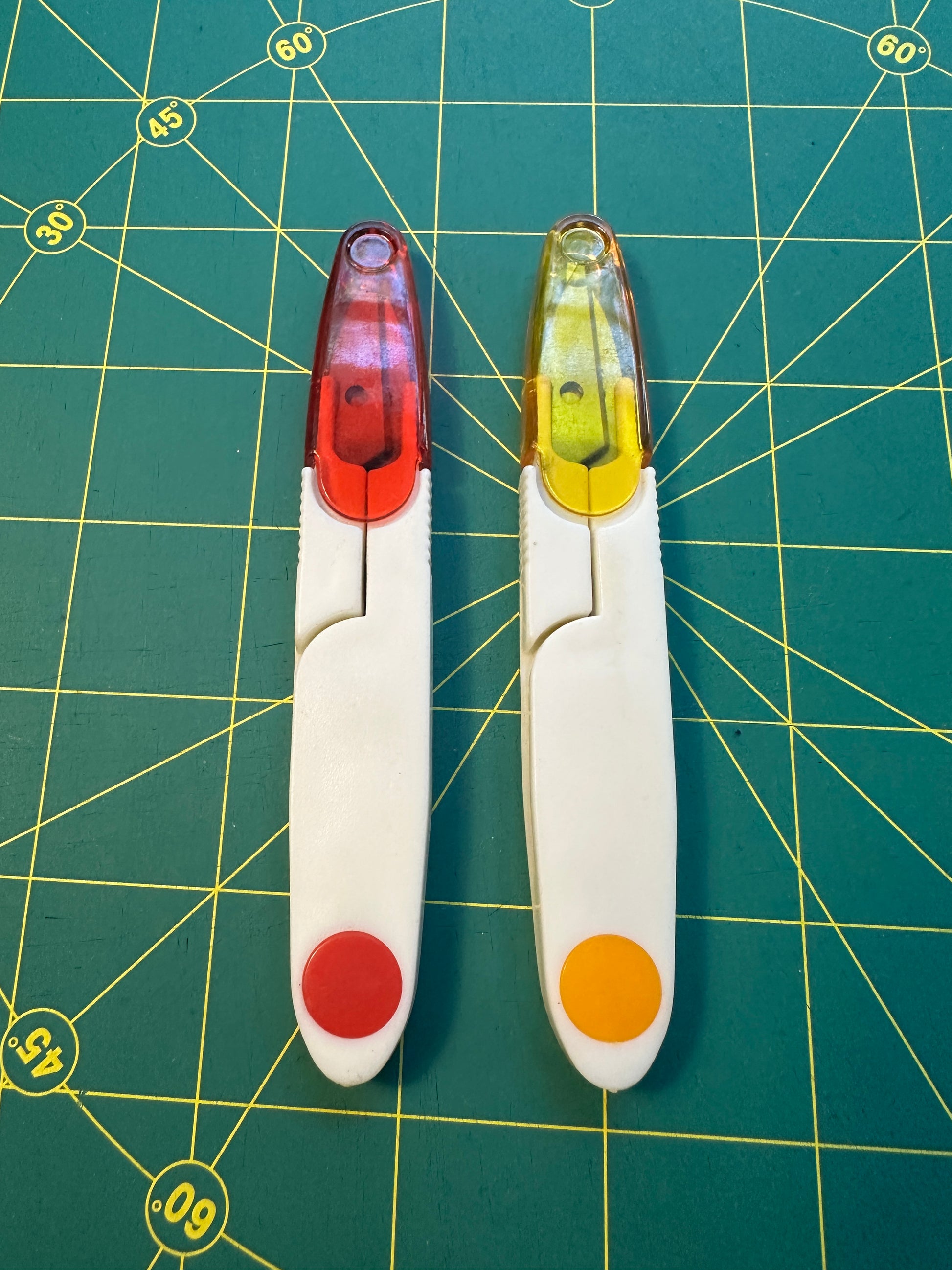 Two small tools with colorful ends on a green cutting mat with grid lines.