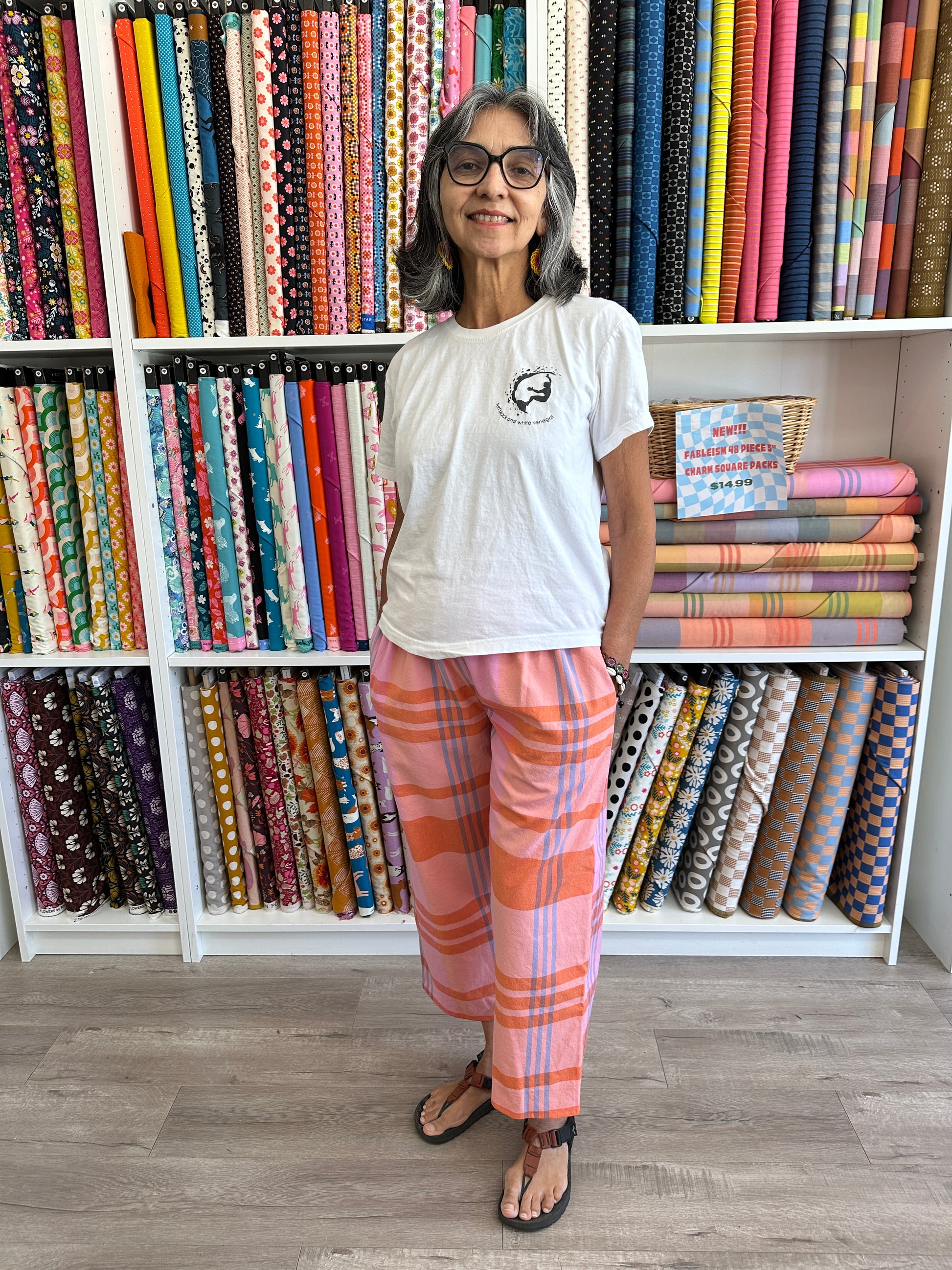 Lana wearing a pair of pink and orange plaid pants in front of a wall of bolts. of fabric
