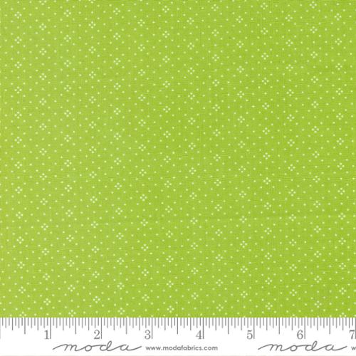 Green fabric with small white polka dots and a ruler at the bottom for scale.