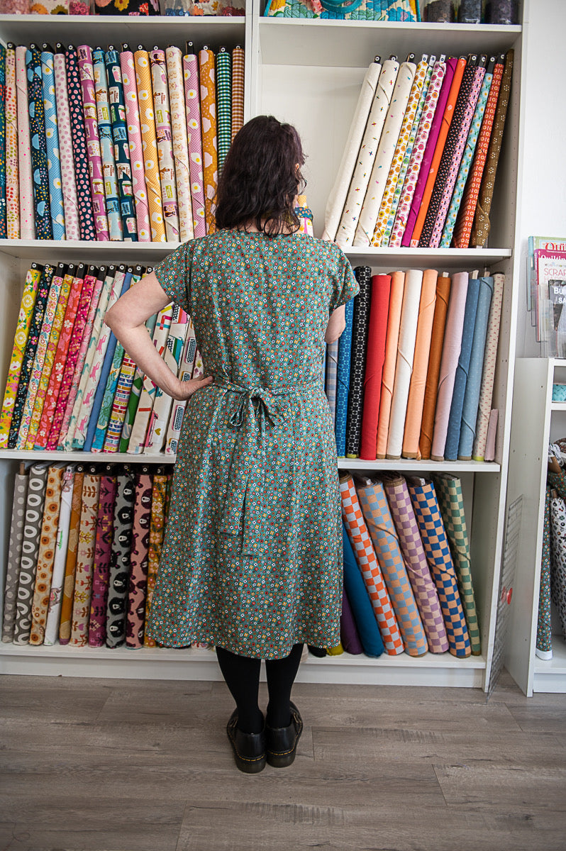 Person in a green dress standing in front of a shelf filled with colorful fabric rolls.