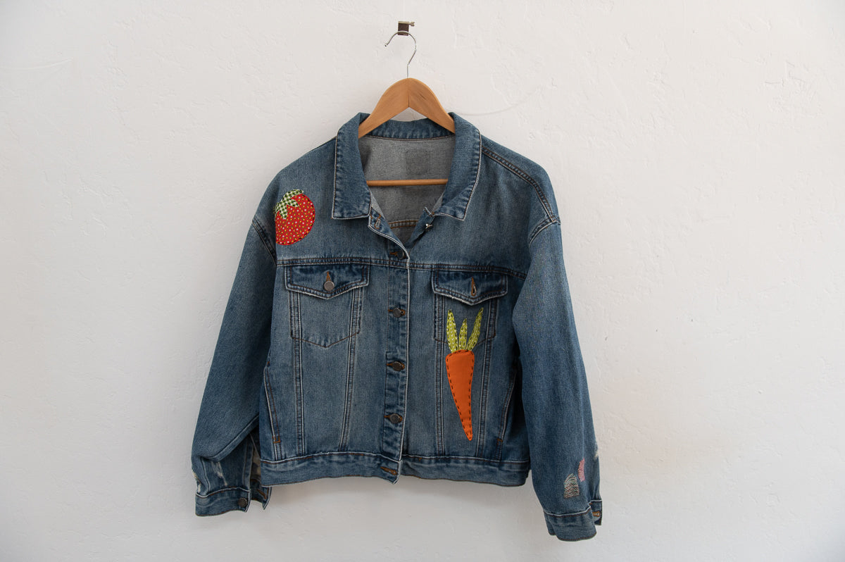Denim jacket with embroidered tomato and carrot designs on a white background