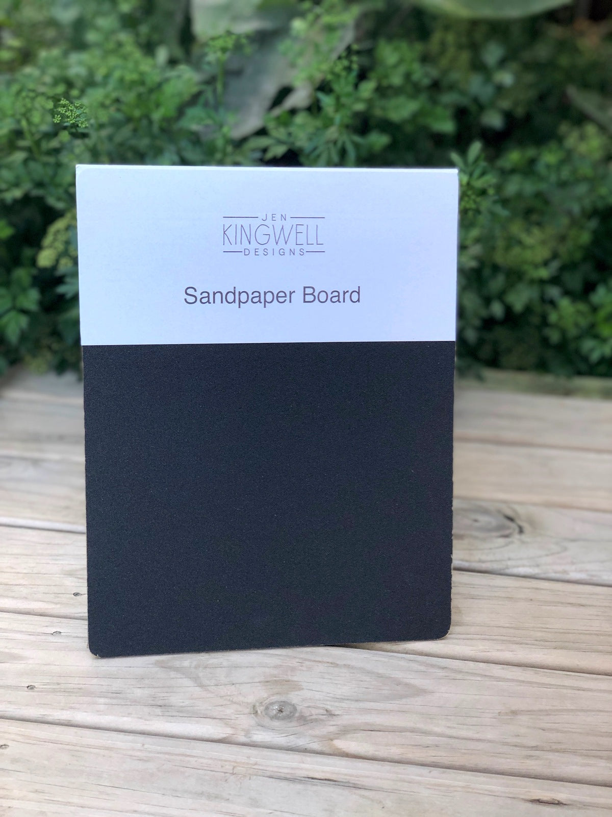 Sandpaper board with Kingwell Designs branding on a wooden surface with greenery in the background