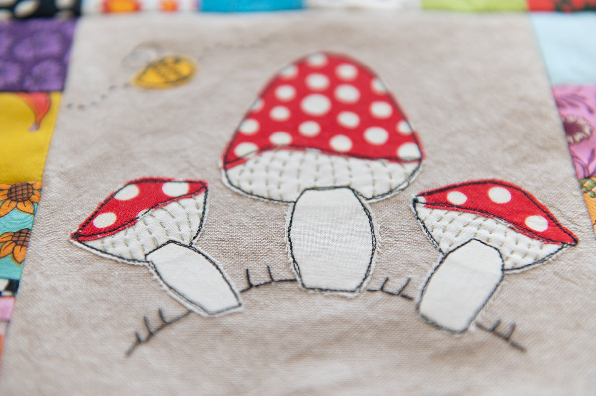 Quilt block with embroidered red and white polka dot mushrooms on a gray background