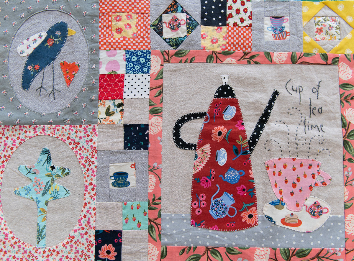 Quilt with a teapot and cup design, surrounded by various patterned squares.