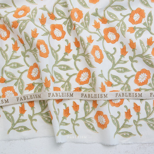 Floral fabric with orange flowers and green leaves on a white background, featuring the brand 'Fableism'.