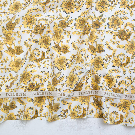 Gold floral pattern on white fabric with 'Fableism' branding.