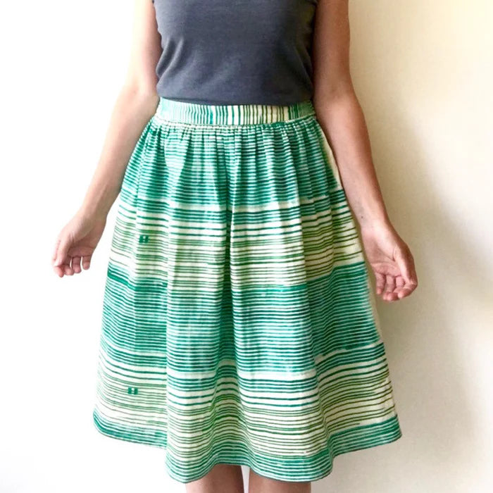 Green and white striped skirt worn by a person on a plain background