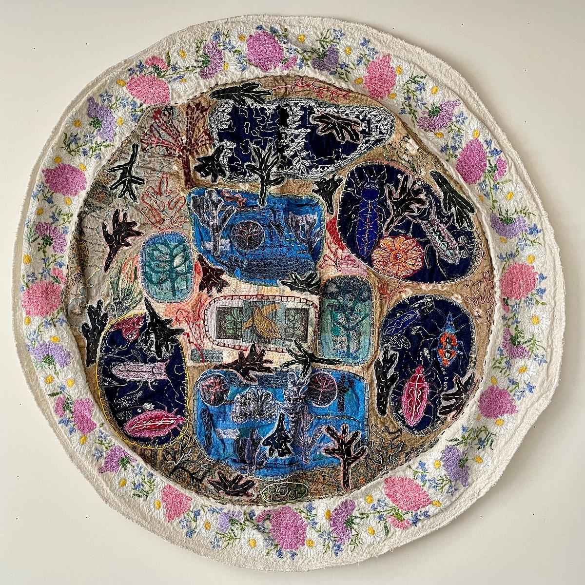textile art with stitched flowers and small creatures