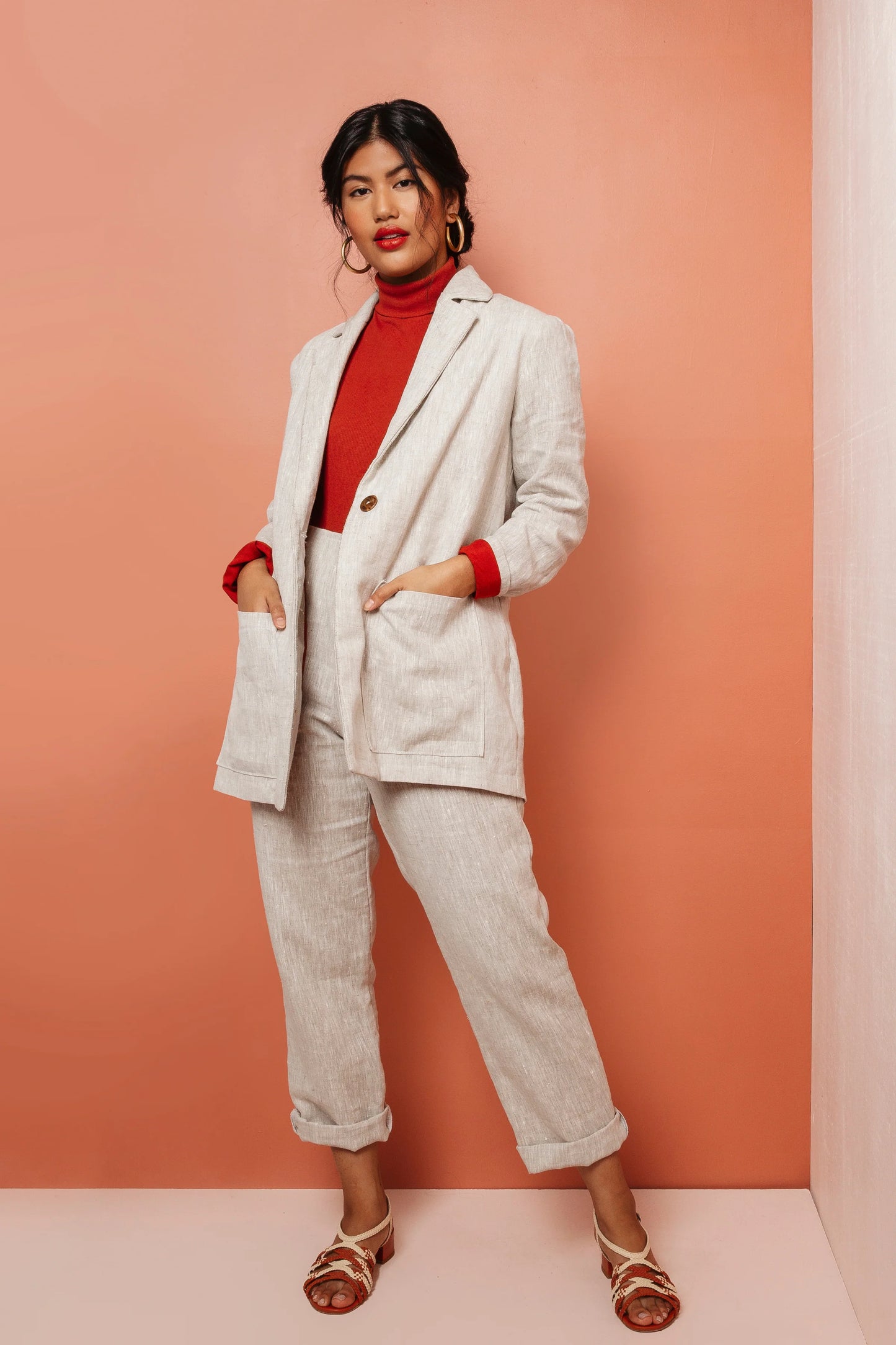Woman wearing a light gray suit with red accents against a peach background