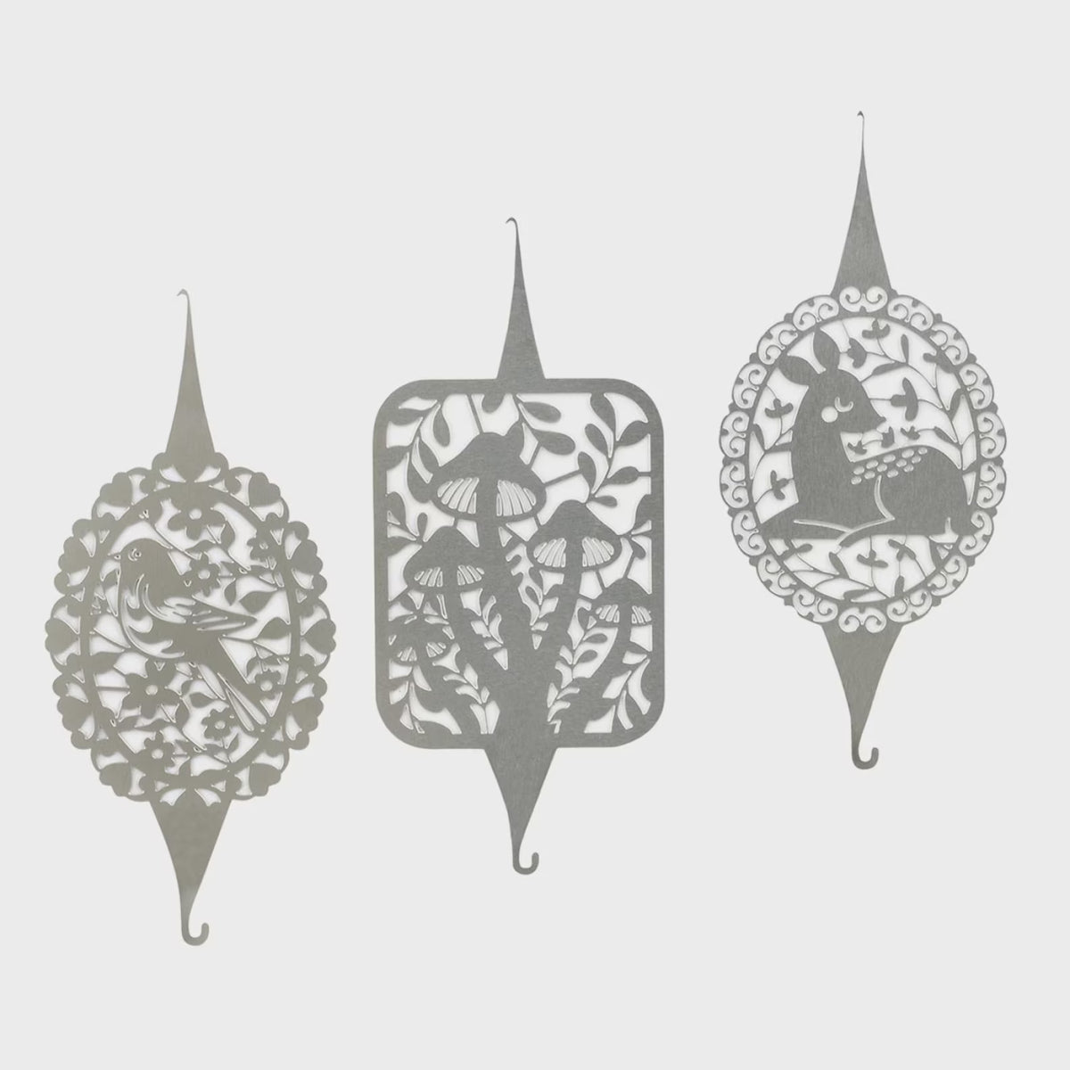 Three decorative needle threaders in a matching gray tone, each with intricate cutout floral and nature motifs including a bird, mushrooms, and a deer, shown against a light gray background.