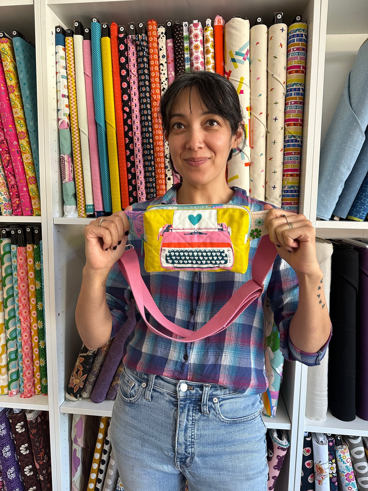 a woman holds a yellow quilted bag in front of a fabric wall