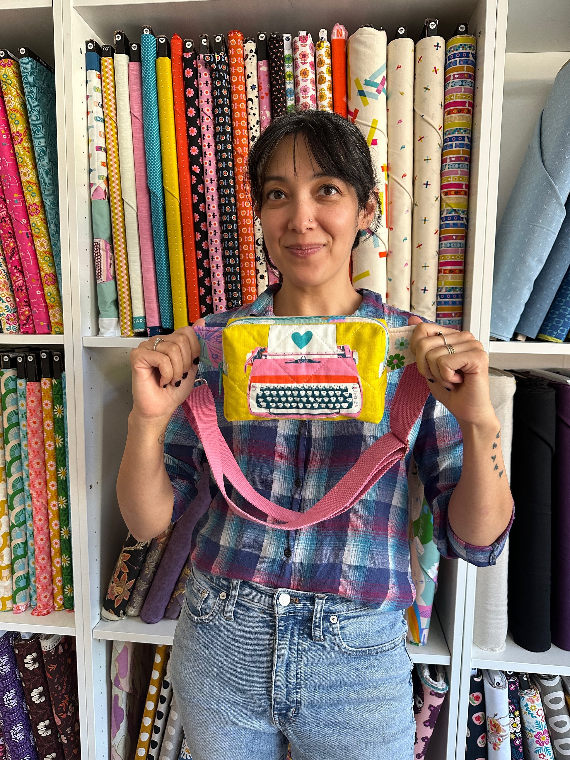 a woman holds a yellow quilted bag in front of a fabric wall