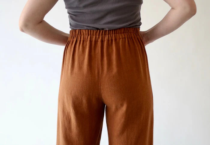 Person wearing rust-colored pants and a gray top against a white background