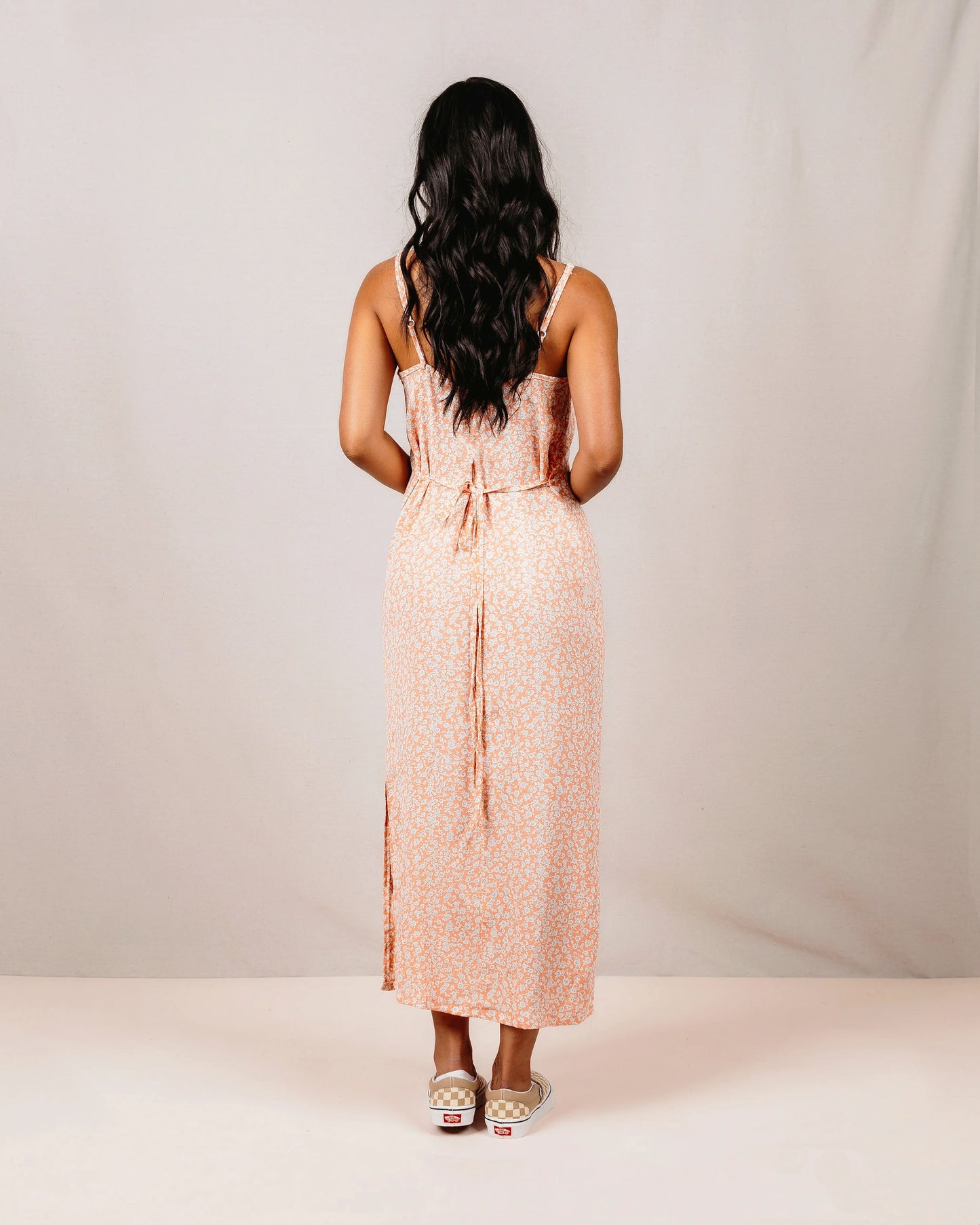 Woman wearing a pink floral dress seen from behind against a plain background