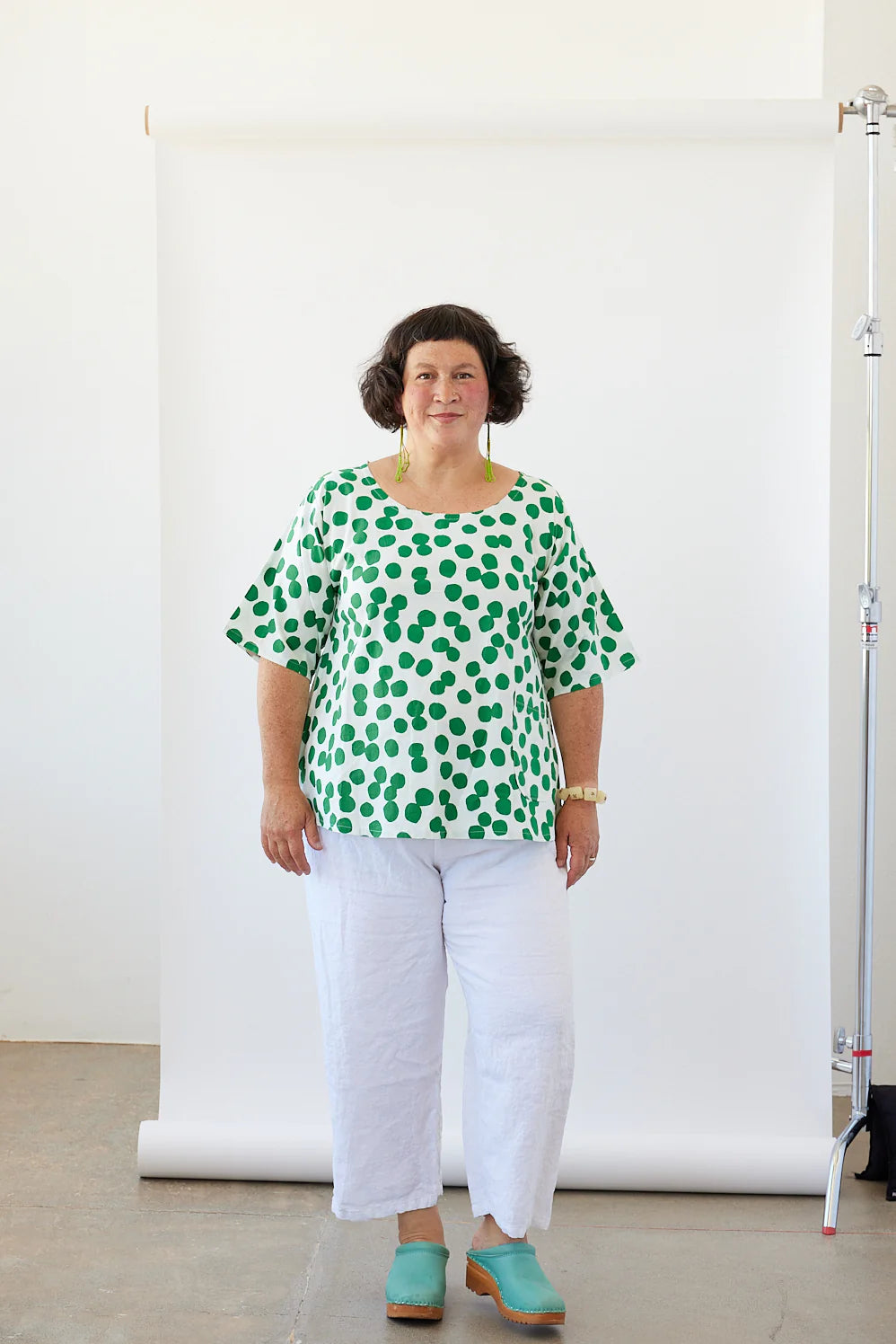 Woman wearing a white tunic with green dots in front of a white background