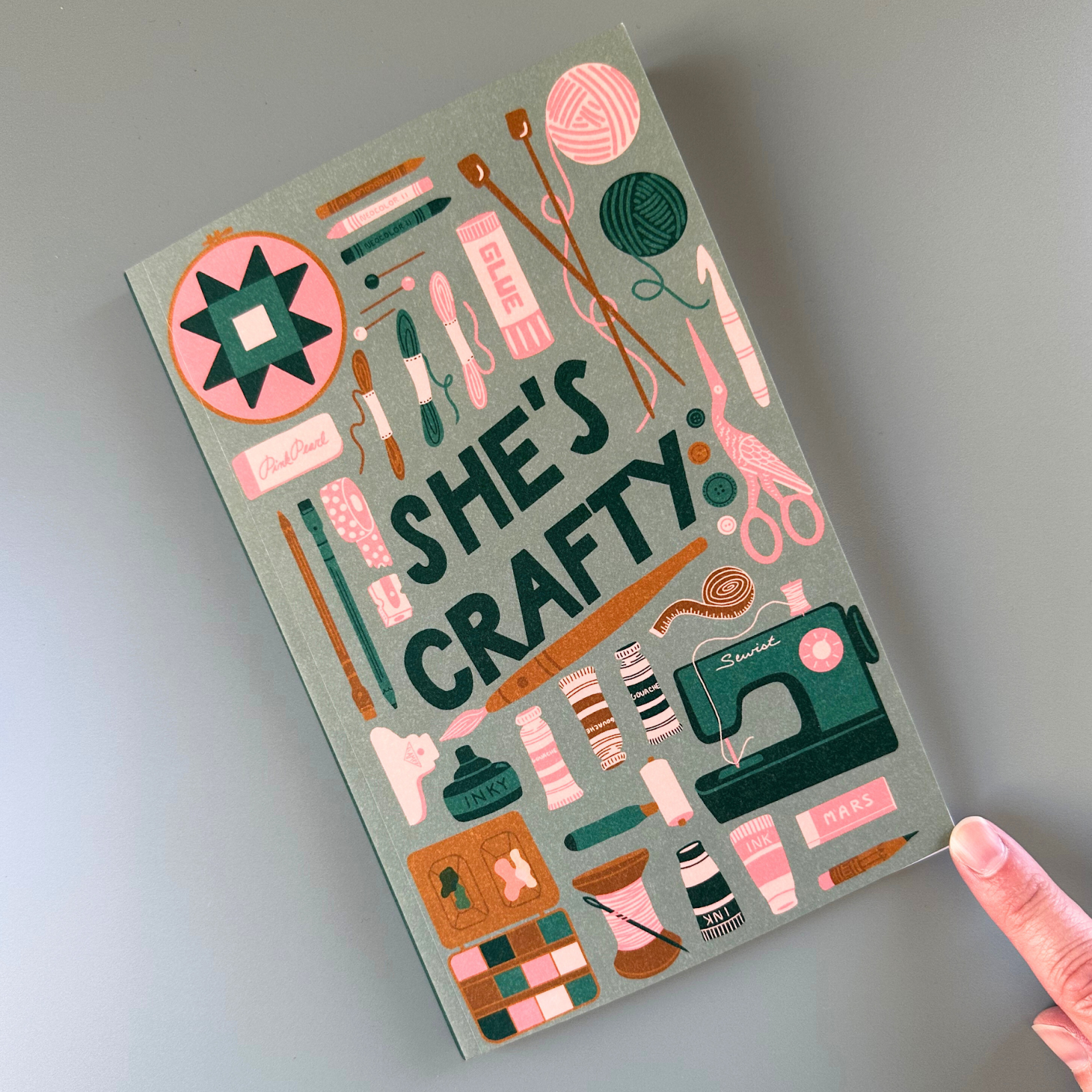 Notebook with 'She's Crafty' design on a gray background