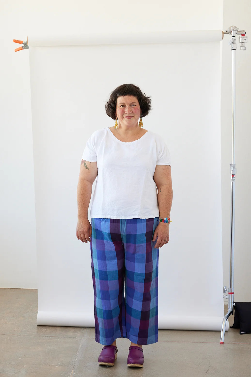 Woman wearing a white shirt and blue plaid pants standing against a white backdrop.