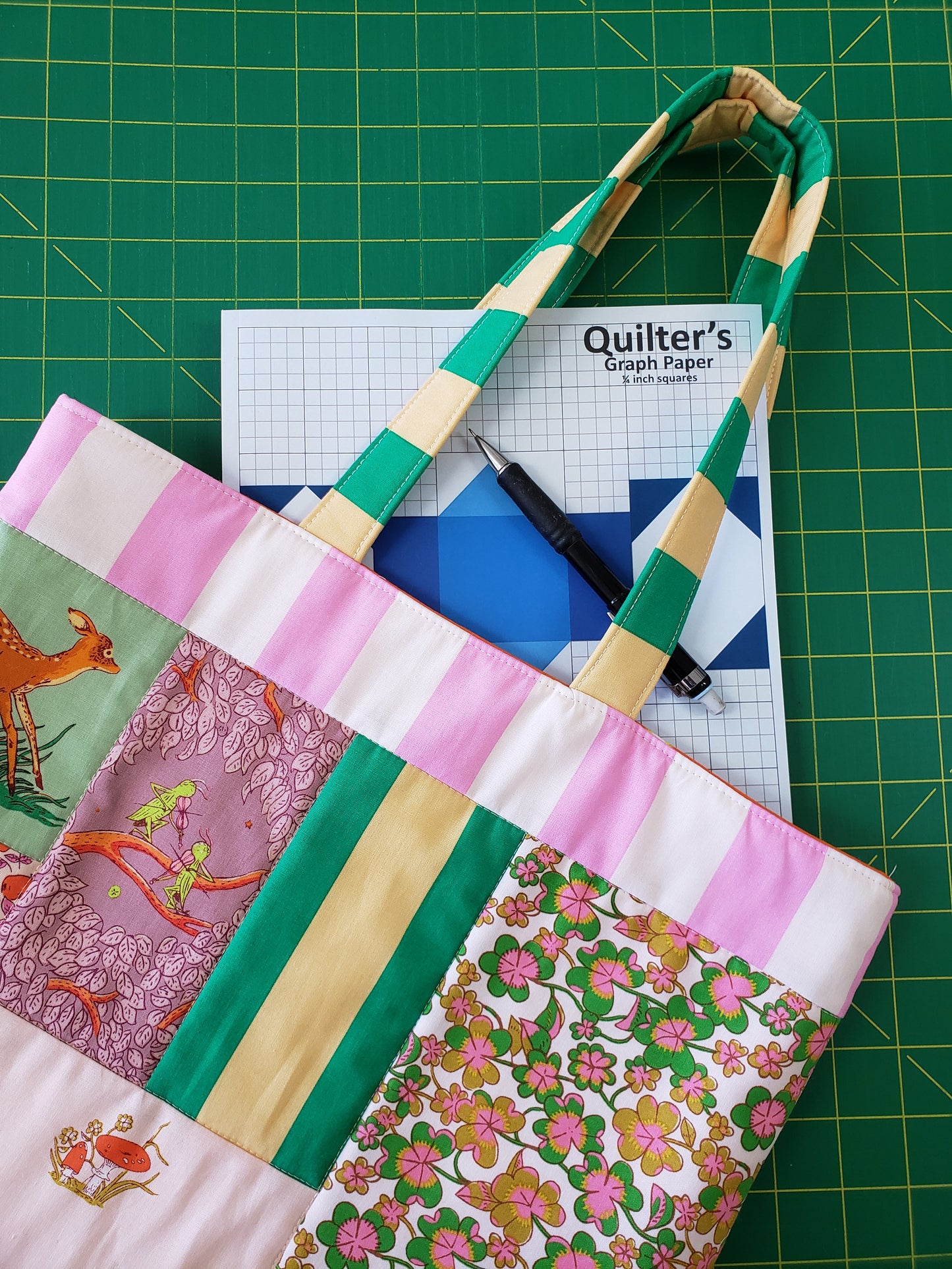 Totebag on a green grid with a pencil and quilter's graph paper pad.