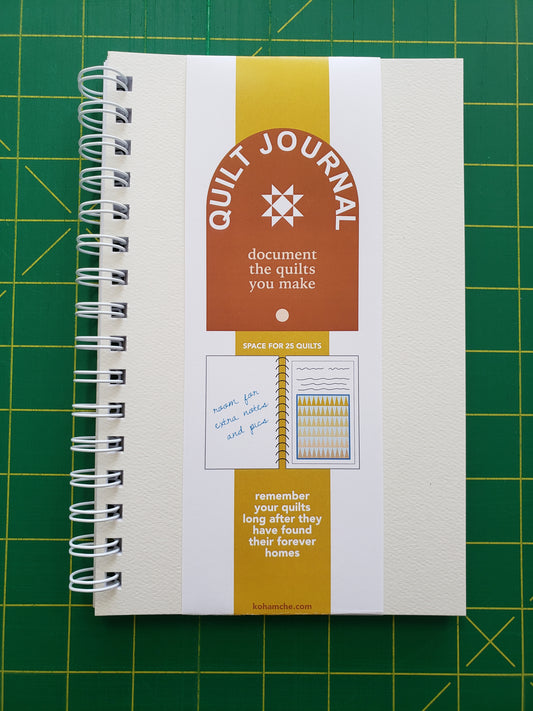 White notebook with descriptive band titled Quilt Journal