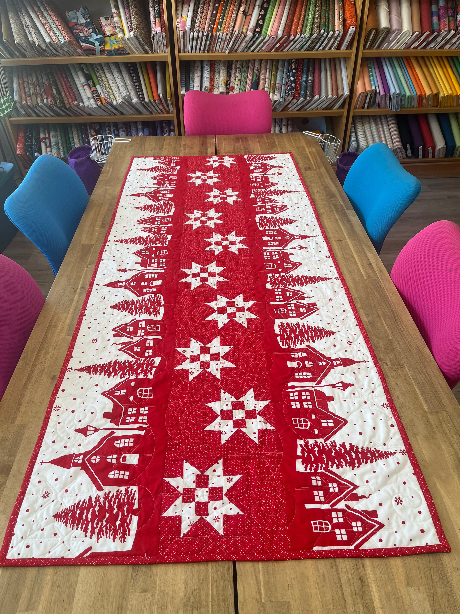 Red table runner with white snowflake and village design on a wooden table.
