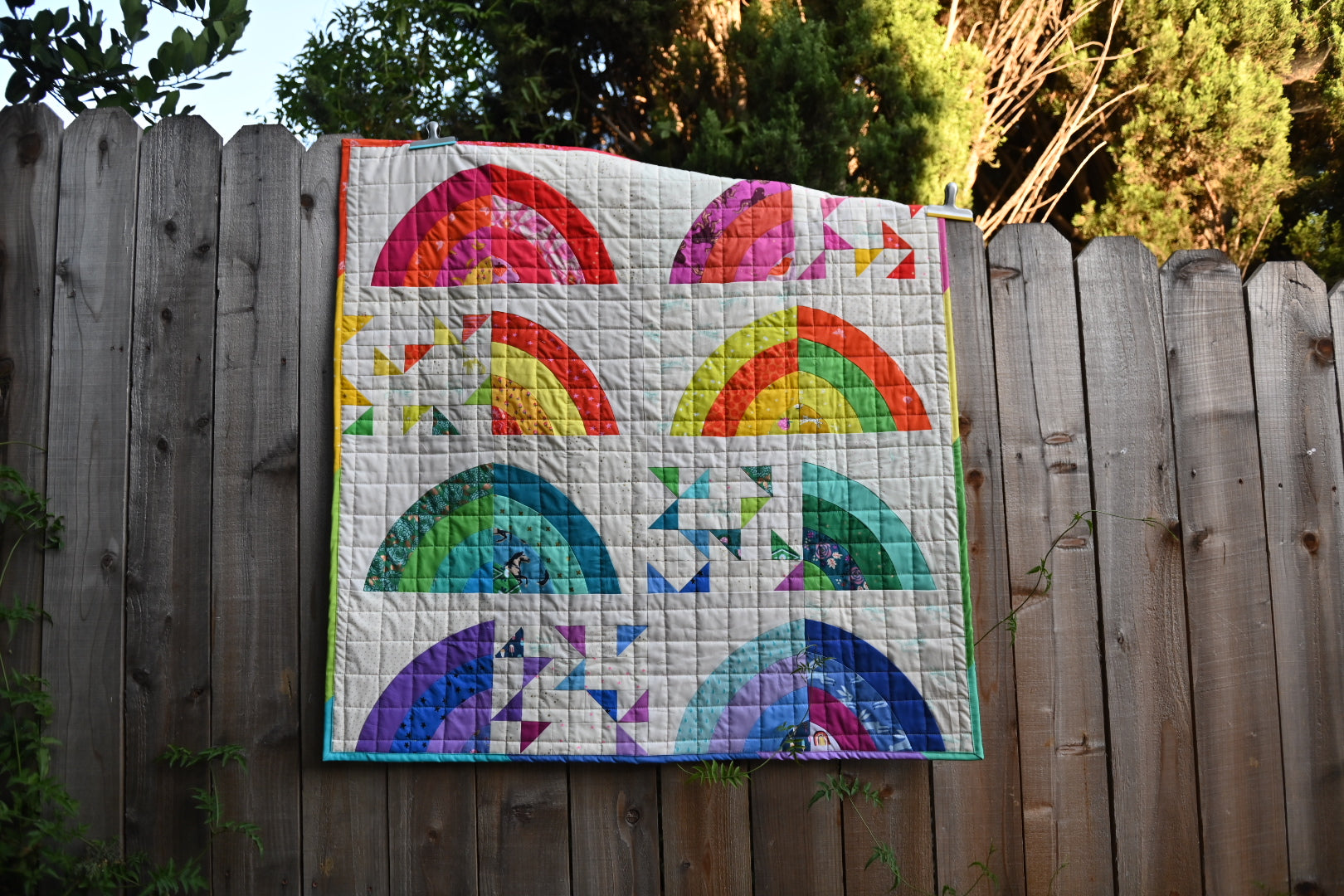Colorful quilt with rainbow and fish patterns hanging on a wooden fence.